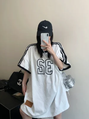 Oversized white varsity jersey tee dress styled with a black baseball cap and silver crossbody bag for Korean streetwear fashion