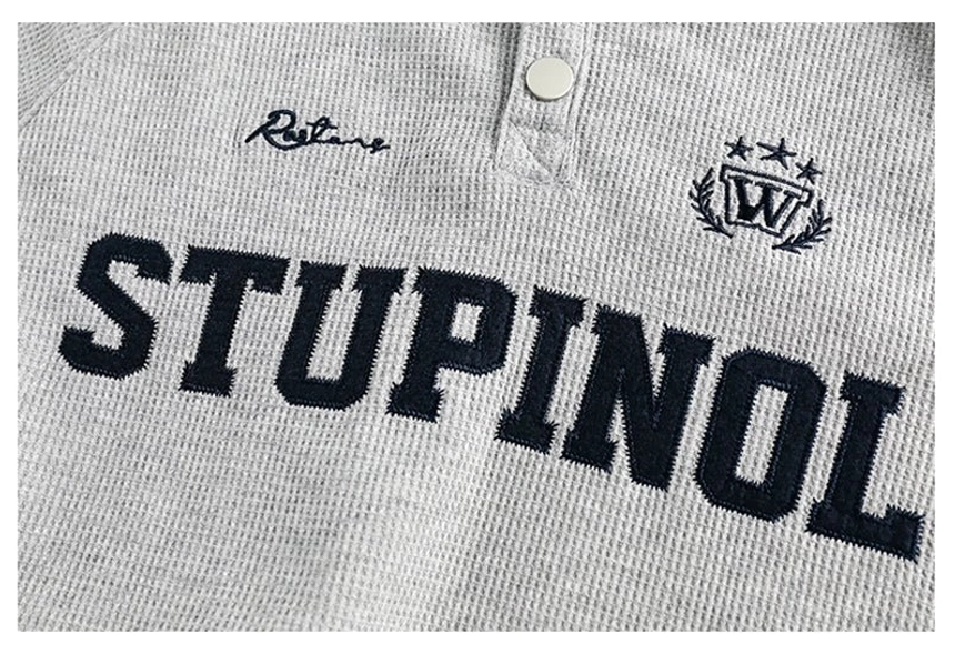 Close-up of textured varsity polo sweatshirt chest featuring embroidered collegiate lettering, crest badge, script detail, and snap placket