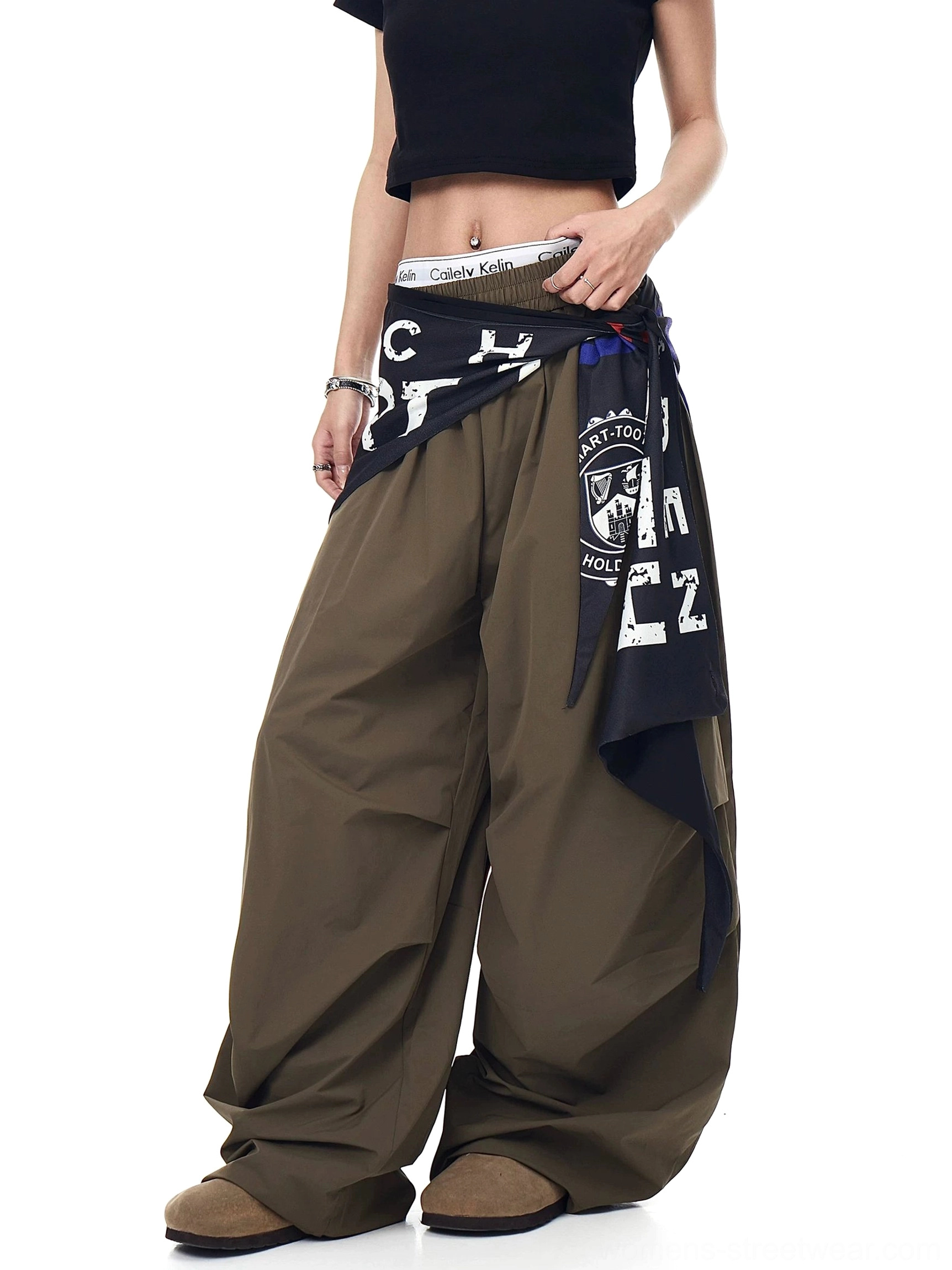 Side front studio view of army green oversized varsity cargo pants with a sculptural puddle hem and detachable scarf accessory