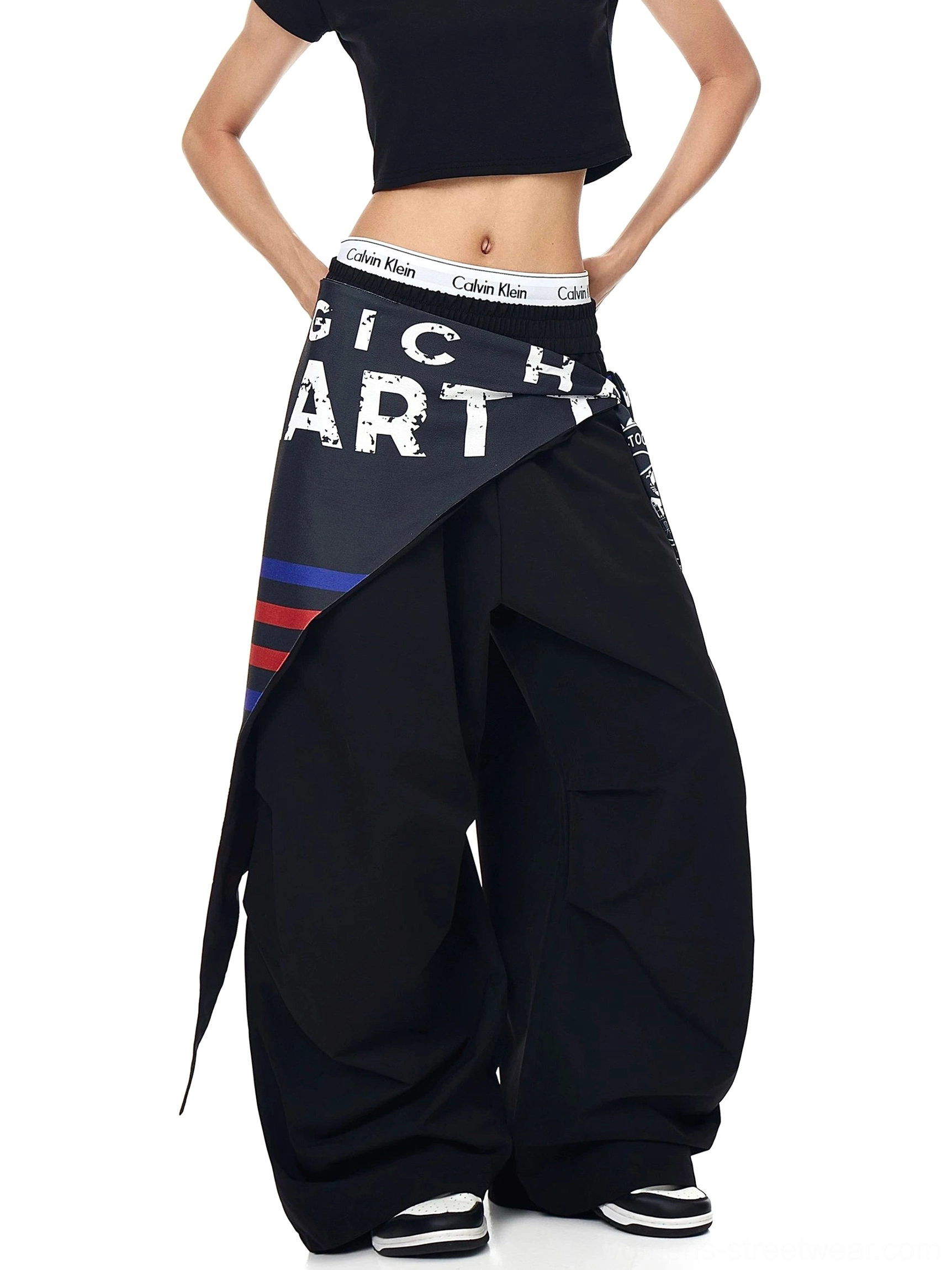Three-quarter back view of black wide-leg streetwear cargo pants with an asymmetric printed varsity scarf, layered texture, and puddle-stacked hem