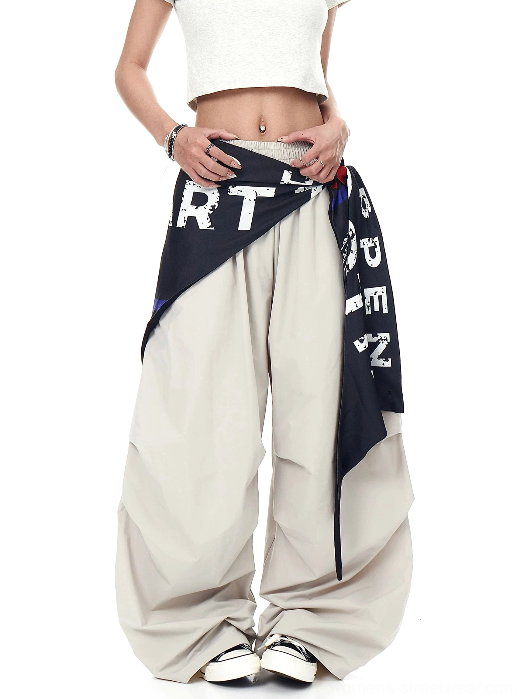 Front view of light beige varsity parachute cargo pants with dramatic wide legs, detachable printed scarf, and white sneaker styling