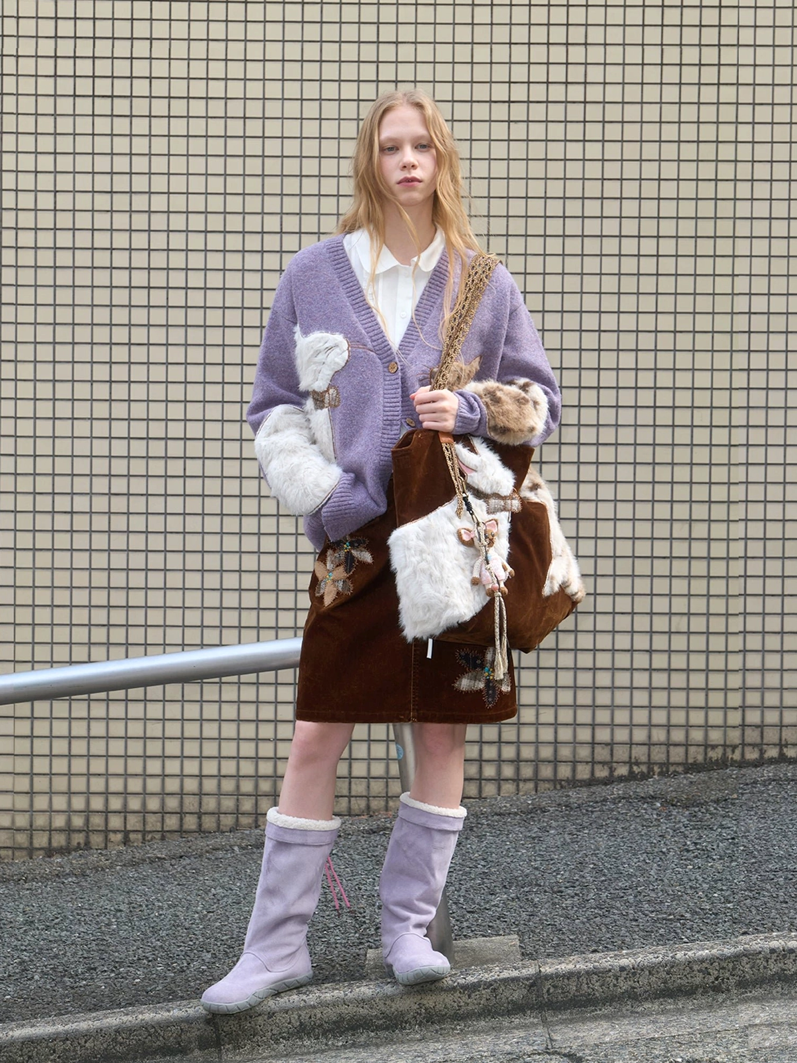 Velvet cat plush crossbody-style tote bag worn with a purple cardigan, corduroy skirt, and lavender boots