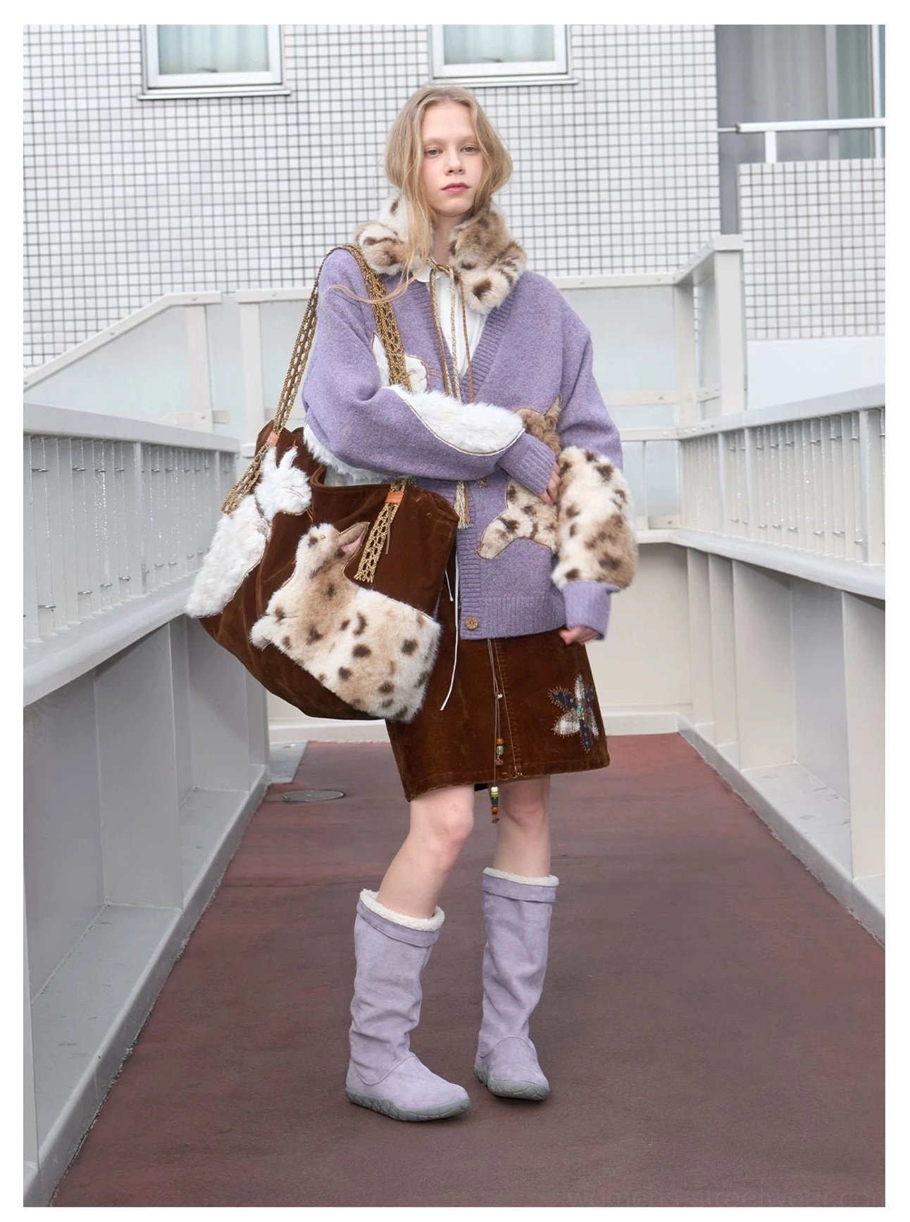 Velvet cat plush tote bag worn over one shoulder with a purple knit cardigan and mini skirt on an urban walkway