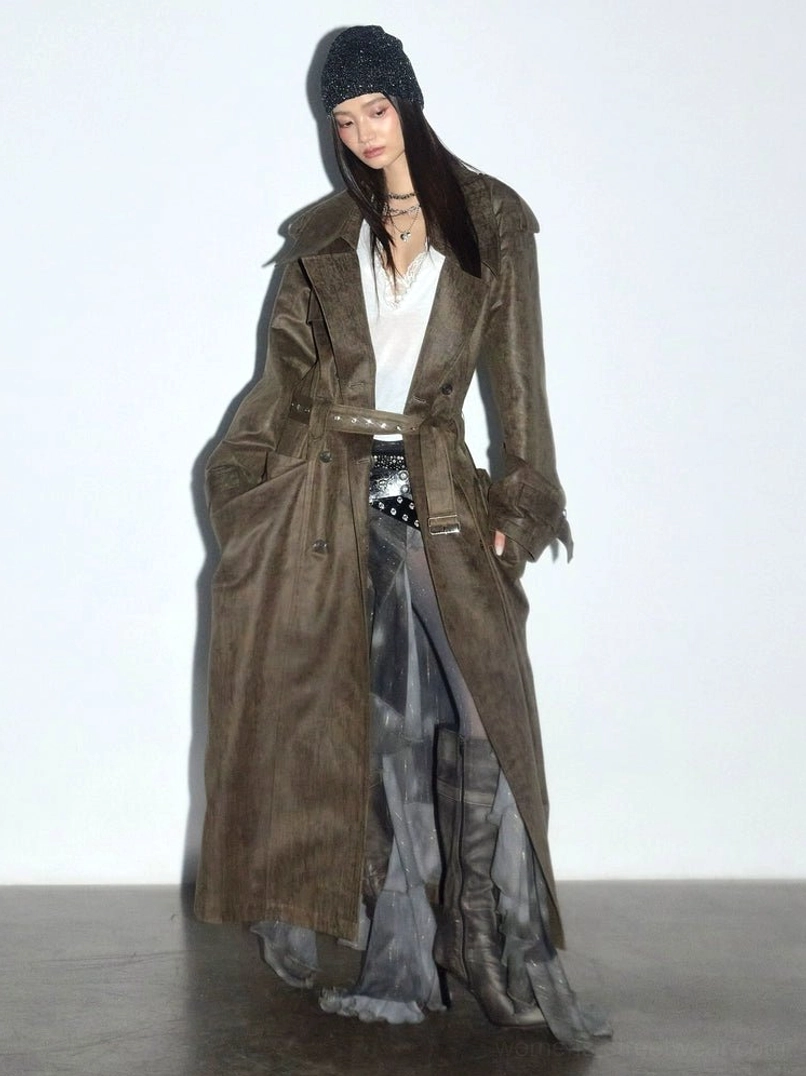 Three-quarter side view of a distressed verdigris olive trench coat with adjustable belt, frayed cuffs, deep pockets, sheer skirt, and ankle boots