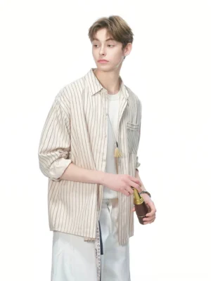Male model wearing a light khaki vertical stripe oversized shirt with rolled sleeves, white T-shirt, and white shorts in a studio