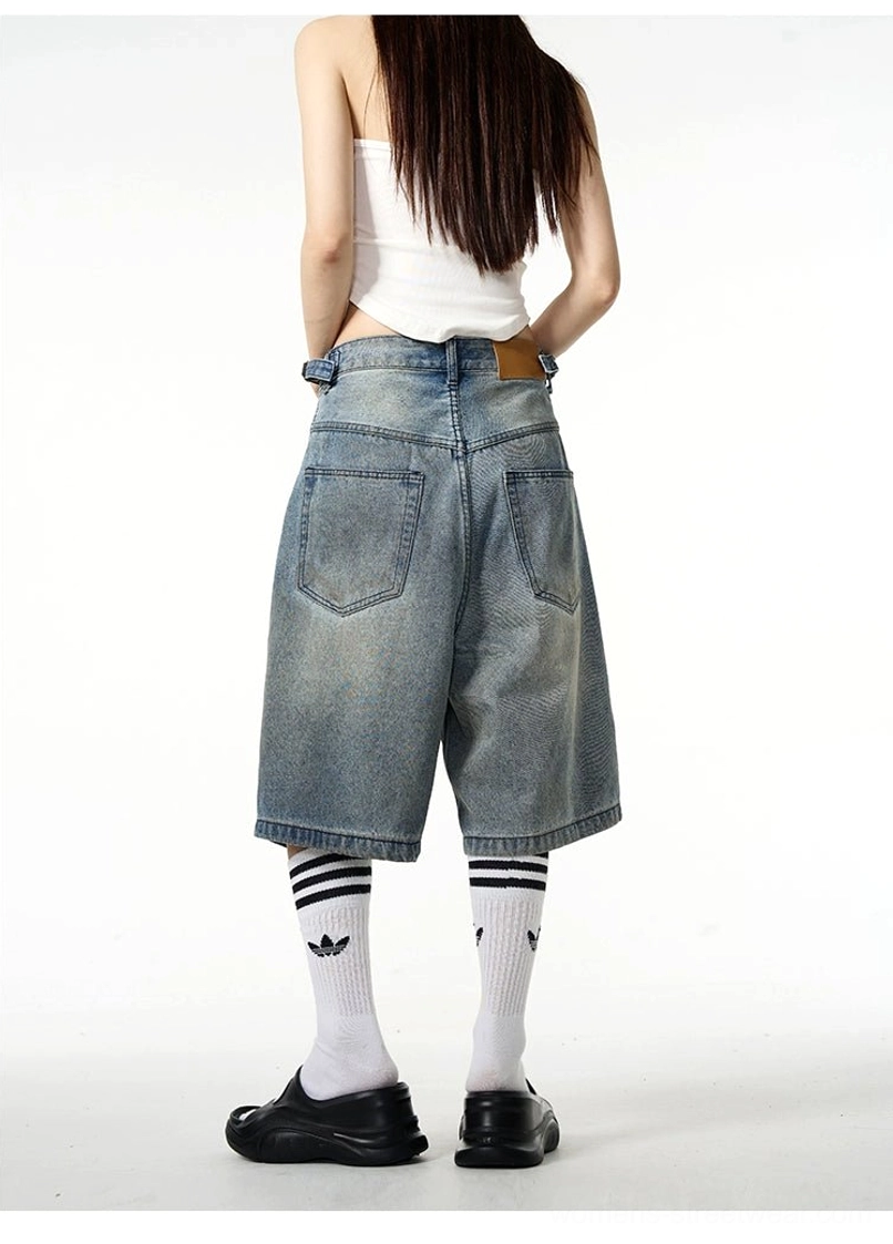 Female model wearing faded blue distressed denim Bermuda shorts showing classic back pockets and oversized streetwear fit