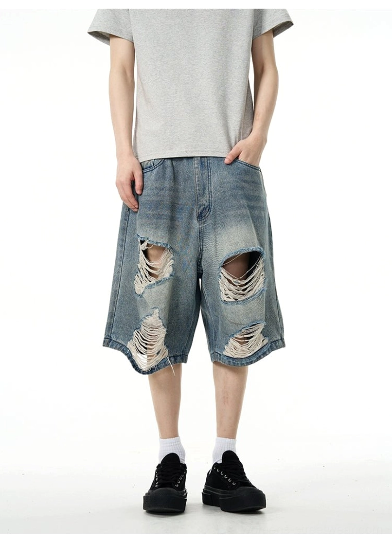 Close front view of faded blue wide-leg distressed denim Bermuda shorts showing large ripped thigh and knee details