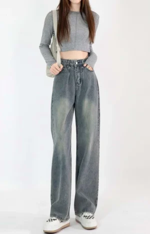 Front full-body view of a woman wearing vintage blue high-waisted faded wide-leg jeans with a cropped gray top and platform sneakers