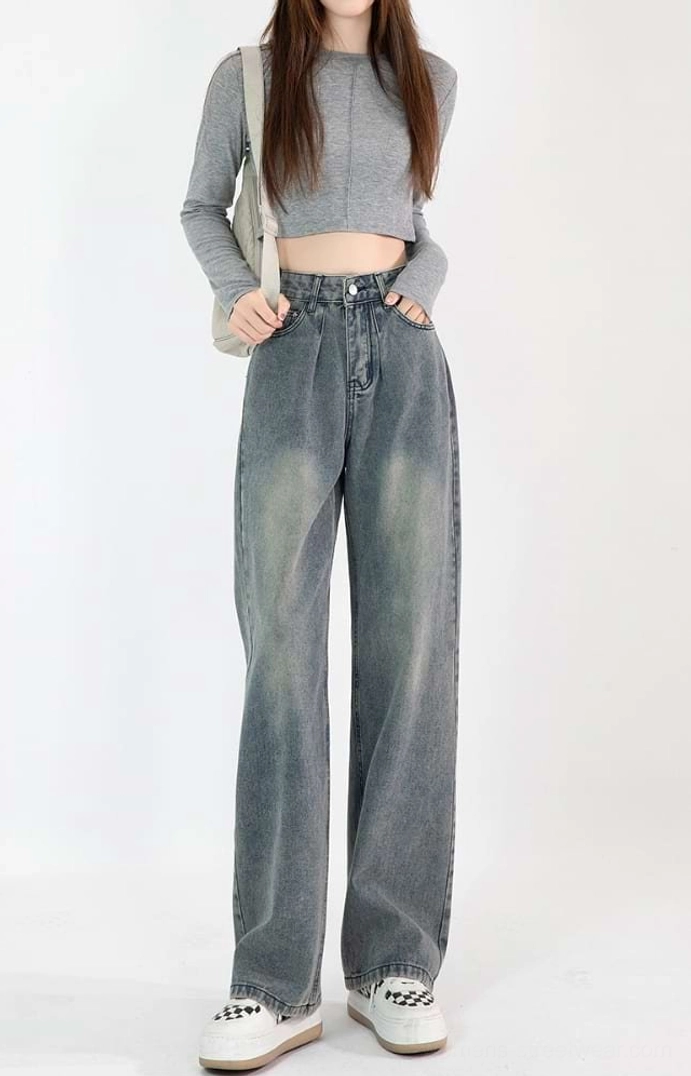 Front full-body view of a woman wearing vintage blue high-waisted faded wide-leg jeans with a cropped gray top and platform sneakers