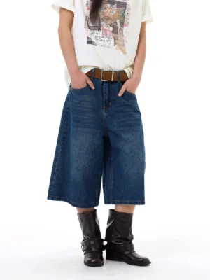 Front full-body view of vintage blue wide-leg denim gaucho shorts styled with a graphic tee, brown leather belt, and black mid-calf boots