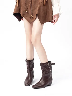 Model wearing vintage brown buckle-cuff western ankle boots with a brown mini skirt front full-leg outfit view