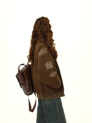 Back view of a vintage brown varsity jacket showing embroidered sleeve badges, contrast shoulder panels, washed fabric texture, elasticated hem, and relaxed oversized streetwear fit