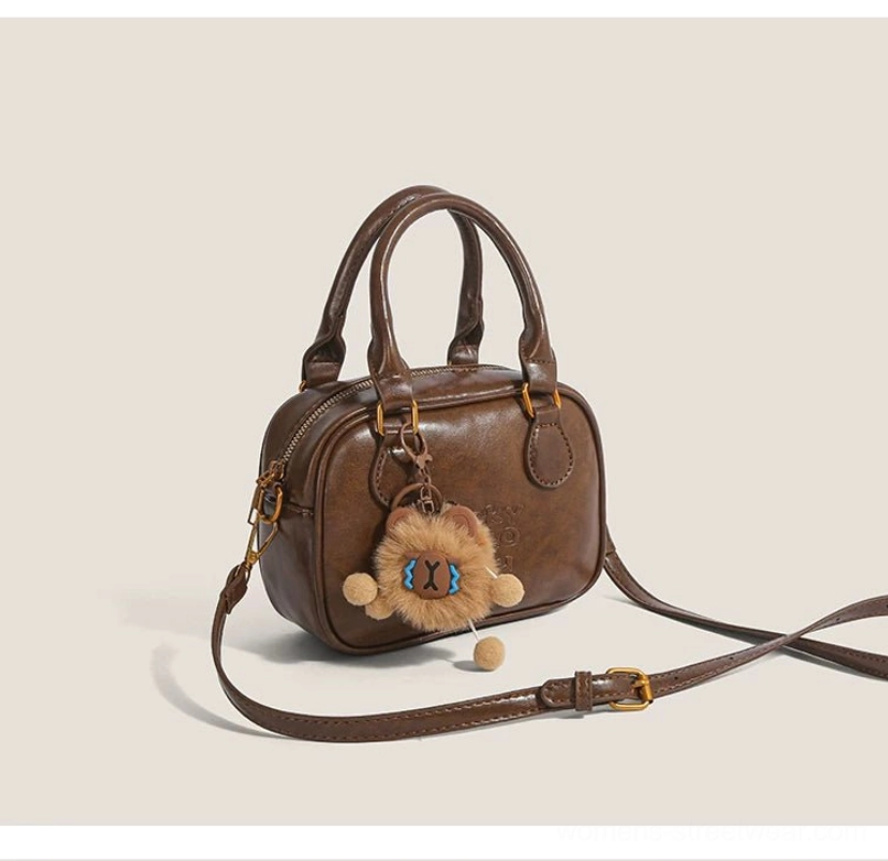 Vintage brown cub charm mini satchel handbag with rounded silhouette, gold side hardware and adjustable crossbody strap