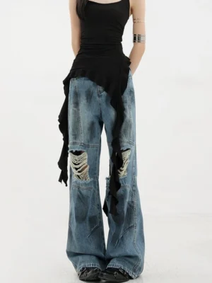 Vintage distressed wide-leg jeans full front view on female model with black ruffled asymmetric camisole showing dirt-dyed faded blue denim knee destruction cuts wide leg fit layered seams