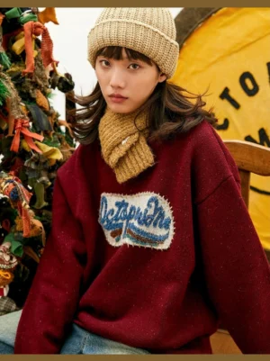 Burgundy vintage-inspired oversized knit sweater with textured embroidered patch, relaxed crewneck streetwear fit, beige knit beanie and scarf styling