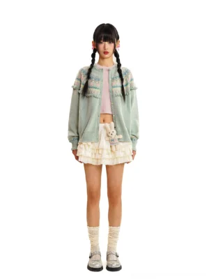 Mint green vintage Fair Isle fringe knit cardigan styled with a pink crop top, ruffled white mini skirt, crew socks, and loafers
