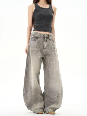 Female model wearing vintage gray paint splatter ultra wide leg denim jeans in a minimalist white studio