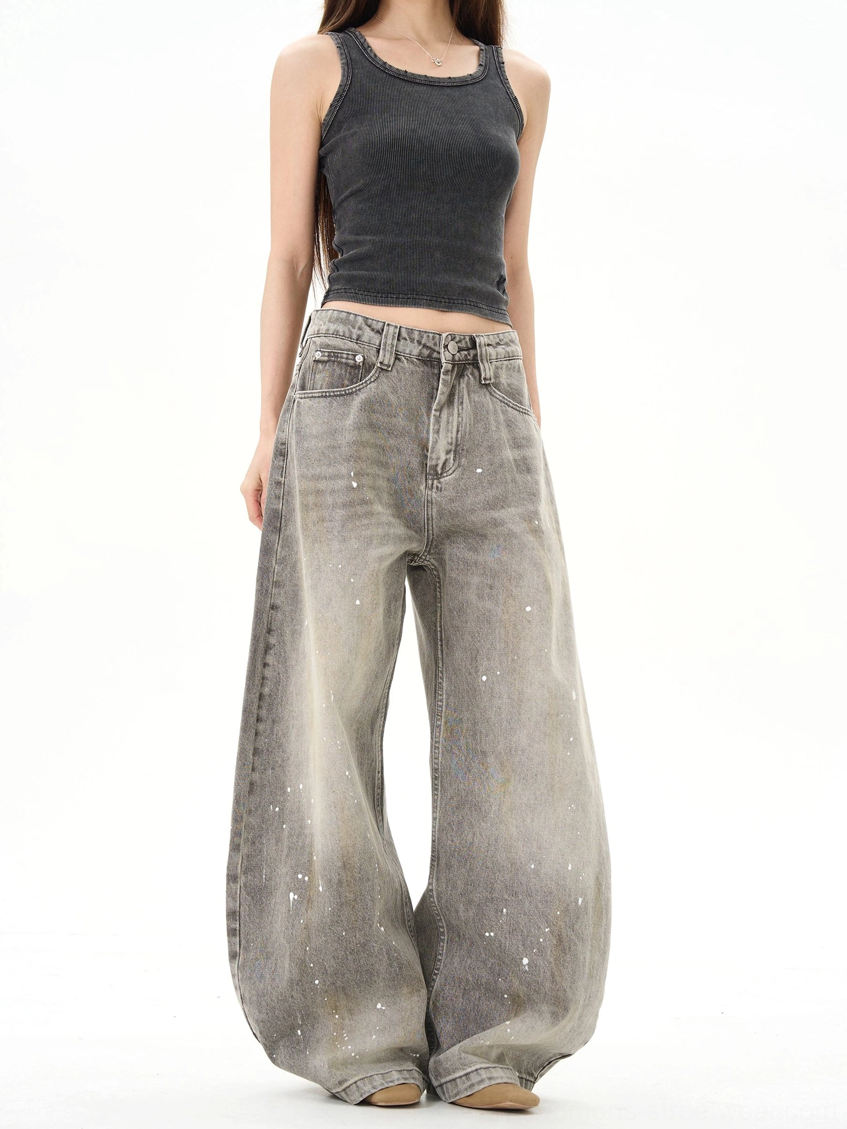Female model wearing vintage gray paint splatter ultra wide leg denim jeans in a minimalist white studio