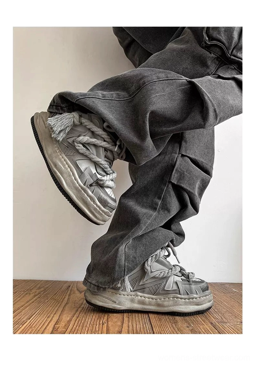 Model wearing vintage grey distressed chunky sneakers with oversized rope laces, thick weathered soles, and dark grey baggy jeans in a casual streetwear outfit