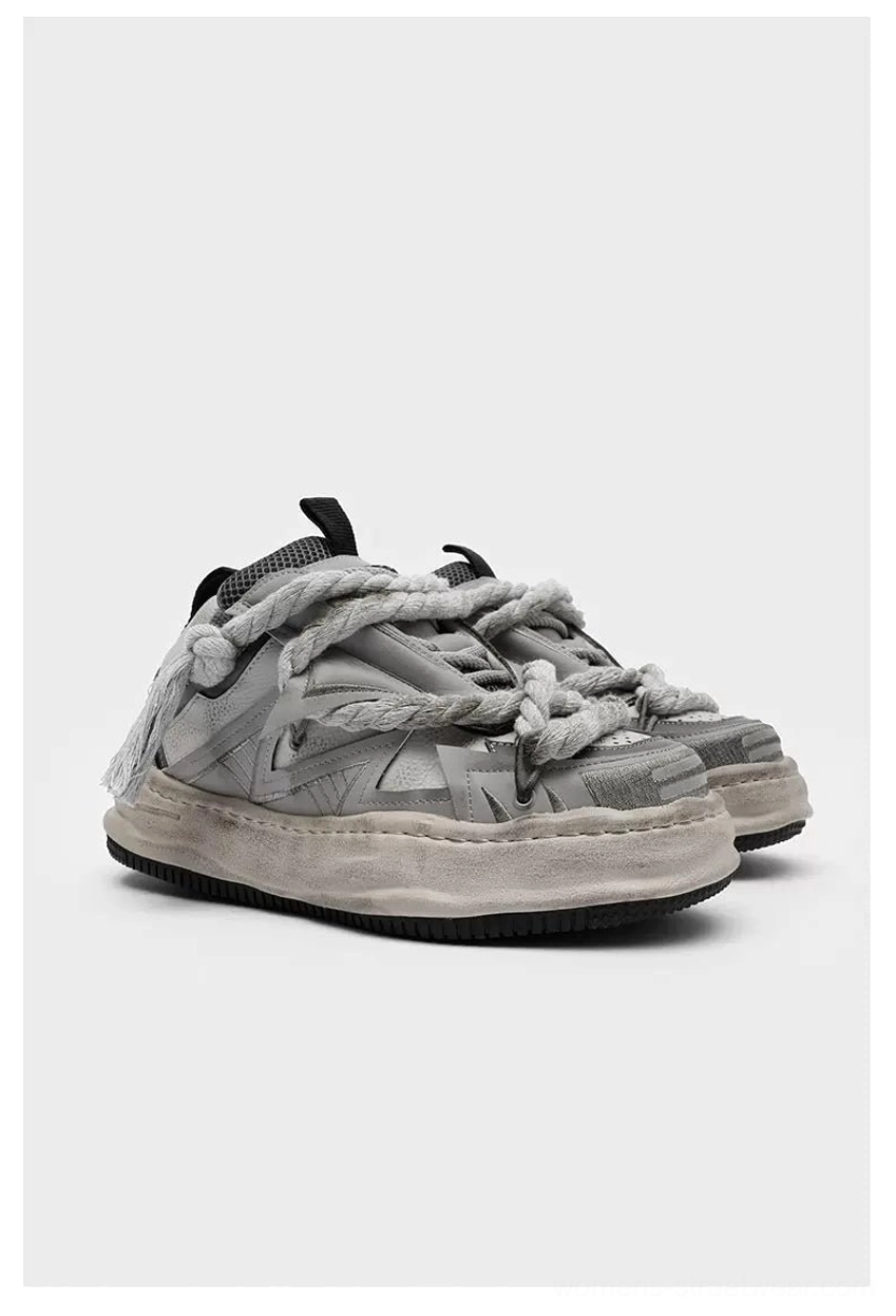 Vintage grey distressed rope-lace chunky sneakers shown in a side three-quarter flat lay with twisted braided laces, faded rubber soles, and mixed leather textile upper details