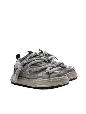 Vintage grey distressed rope-lace chunky sneakers shown from a side three-quarter view with twisted tassel laces, mixed mesh and microfiber leather panels, and a faded chunky rubber sole