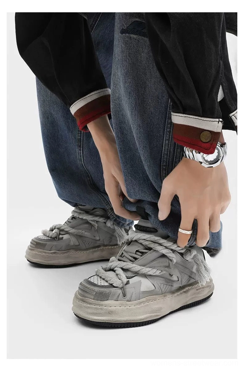 Front low-angle view of vintage grey distressed rope-lace chunky sneakers worn with baggy denim pants, matching braided laces, and thick weathered streetwear soles