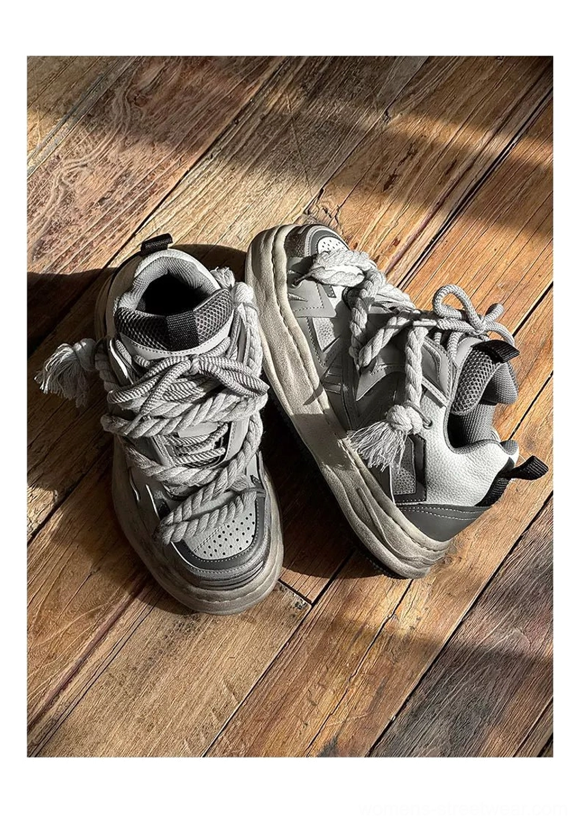Top-down view of vintage grey distressed rope-lace chunky sneakers on a wooden floor, showing braided laces, mixed textile and leather panels, and weathered platform midsoles
