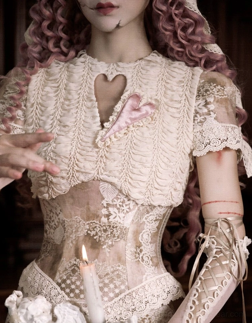 Close-up of a vintage lace corset top neckline featuring a heart cutout, pink satin heart decoration, ruched cream fabric, and delicate trim
