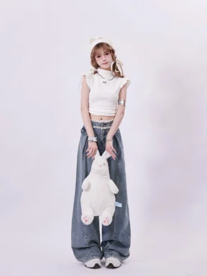 Front full-body view of faded blue vintage lace waist pleated wide-leg denim jeans styled with a white cropped ruffle top and sneakers