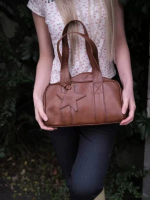 Brown polyurethane vintage star bowling handbag styled with floral top and dark wash jeans in an outdoor garden setting