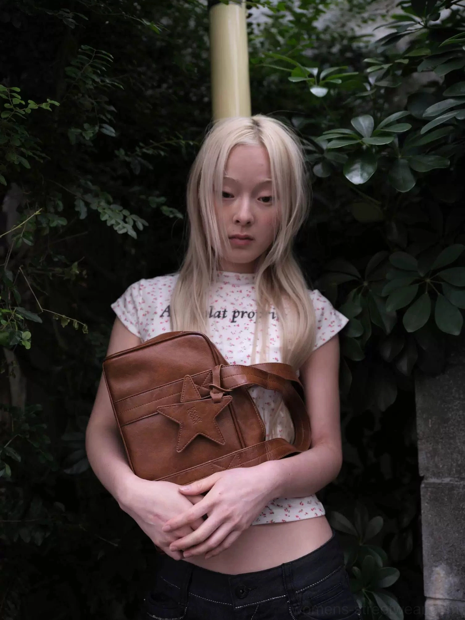 Chestnut brown vintage star east-west bowling handbag carried by model outdoors with twin top handles and hanging star charm