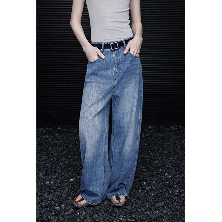 Low angle front view of women’s vintage wash barrel leg jeans with full length faded blue denim and curved wide leg fit