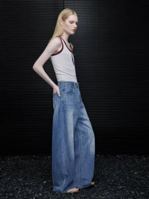 Side view of women’s faded blue barrel leg jeans showing the curved wide leg silhouette and full length denim drape