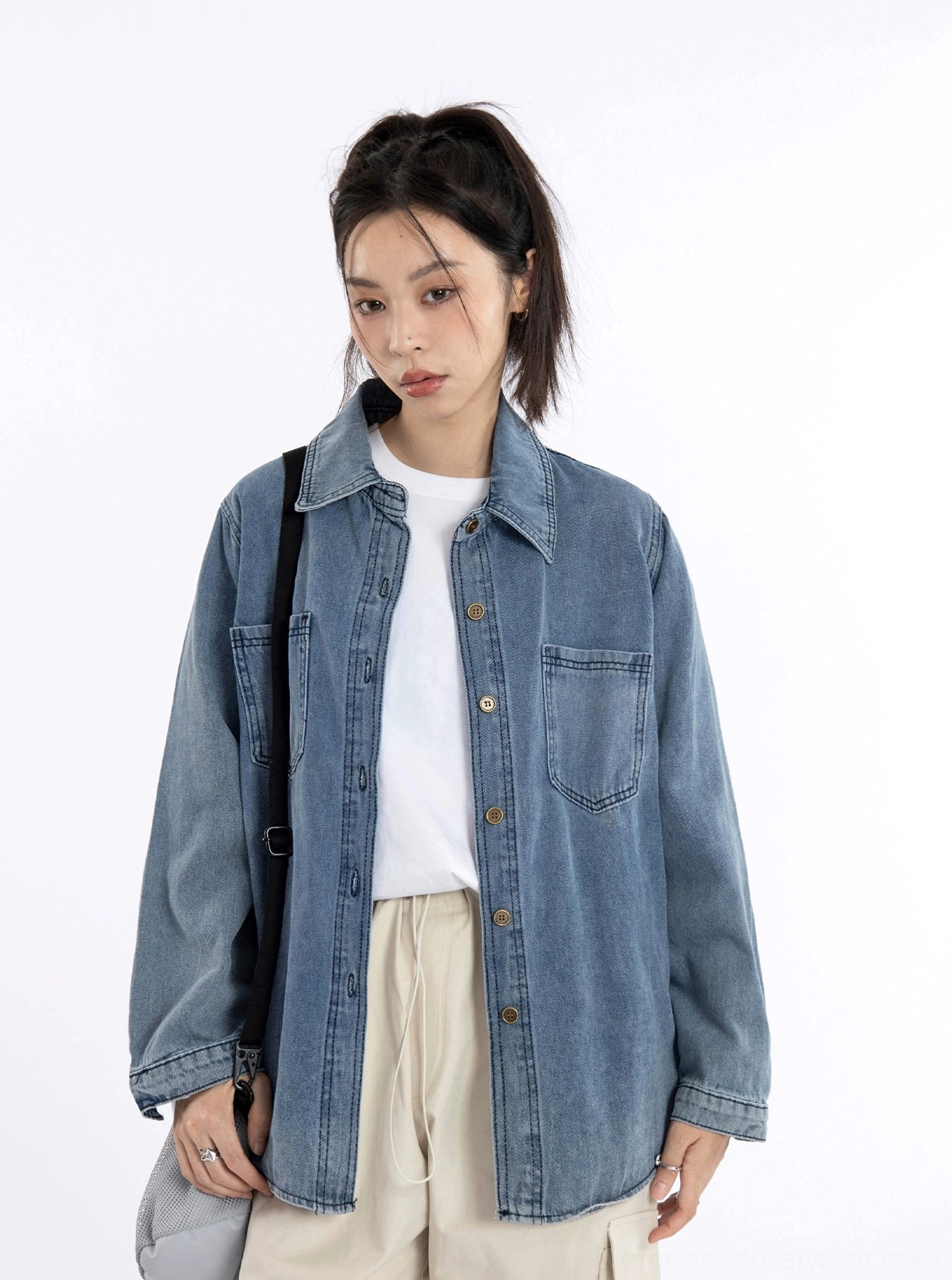 Close-up of a vintage washed blue denim shirt jacket layered over a white basic tee with beige casual trousers