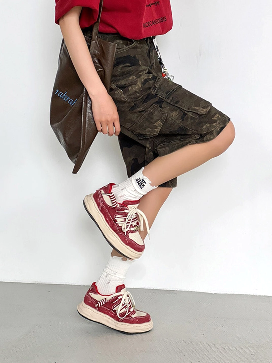 Vintage washed denim sneakers styled with camo cargo shorts, a cropped red top, and a leather tote in a Y2K streetwear outfit