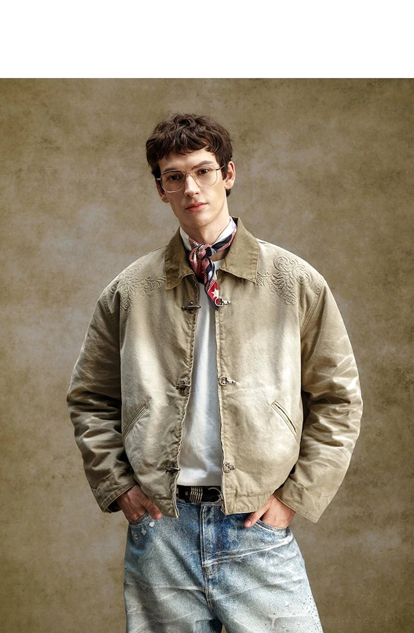 Male model wearing a vintage washed khaki embroidered toggle jacket with contrast collar, scarf, tee, and wide-leg denim