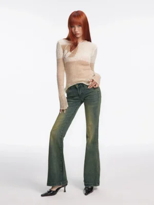 Full-body front view of a model wearing vintage washed low-rise flared jeans with a faded blue-green denim finish, beige sheer long-sleeve top, and pointed heels