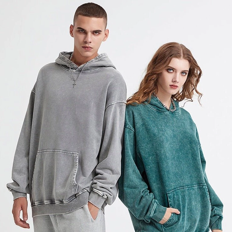 Light gray and teal green vintage washed oversized hoodies worn by models with kangaroo pockets and drawstring hoods