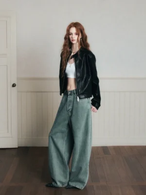 Three-quarter side view of vintage washed wide-leg jeans styled with a black cropped leather jacket and white tank top in a retro indoor setting