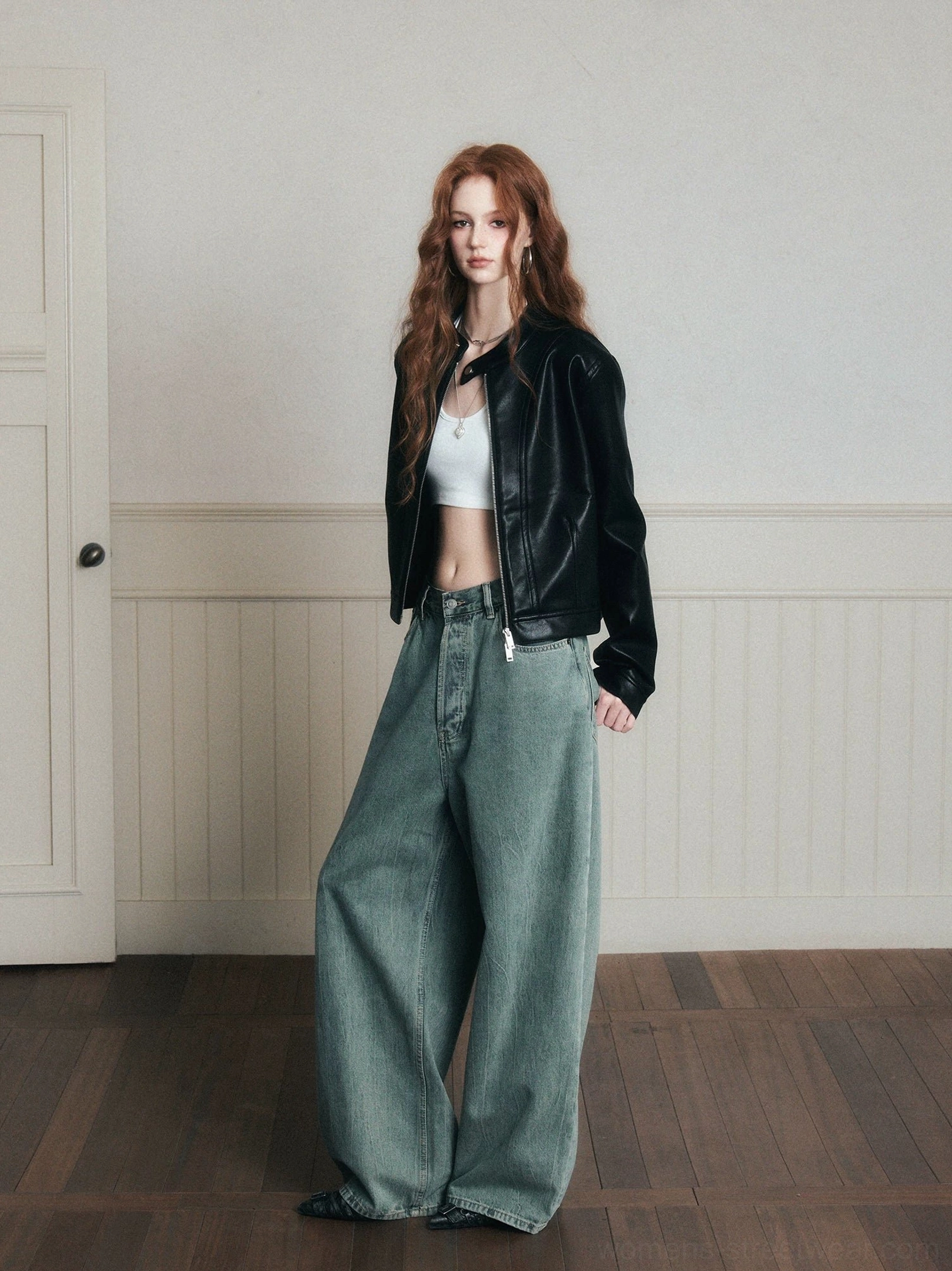 Three-quarter side view of vintage washed wide-leg jeans styled with a black cropped leather jacket and white tank top in a retro indoor setting