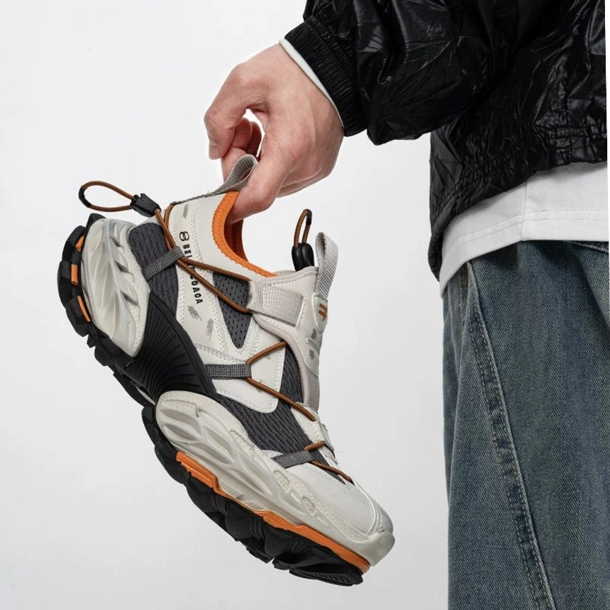 Grey orange and black mesh tech trail sneakers in a clear three quarter view showing multi-panel breathable construction, orange inner lining, utility straps, and bold chunky streetwear silhouette