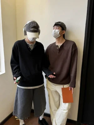 Two male models wearing waffle knit Henley shirts with half-button collars and faux layered hems in a relaxed streetwear entryway setting
