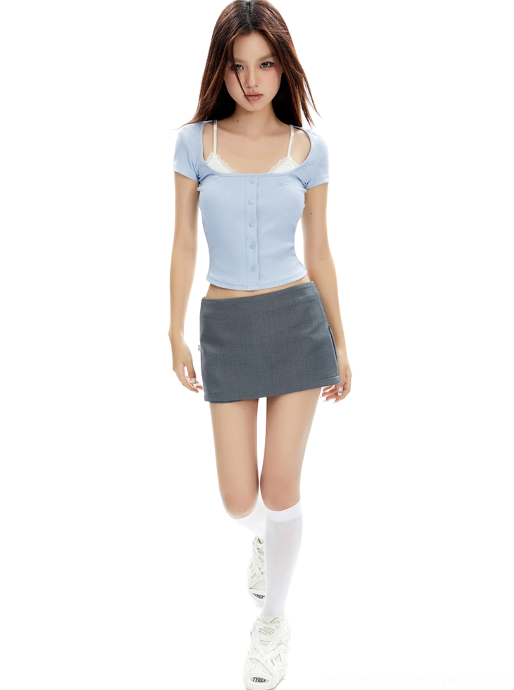 Model walking in a low-rise gray mini skirt with side slit, cropped blue top, and white knee-high socks