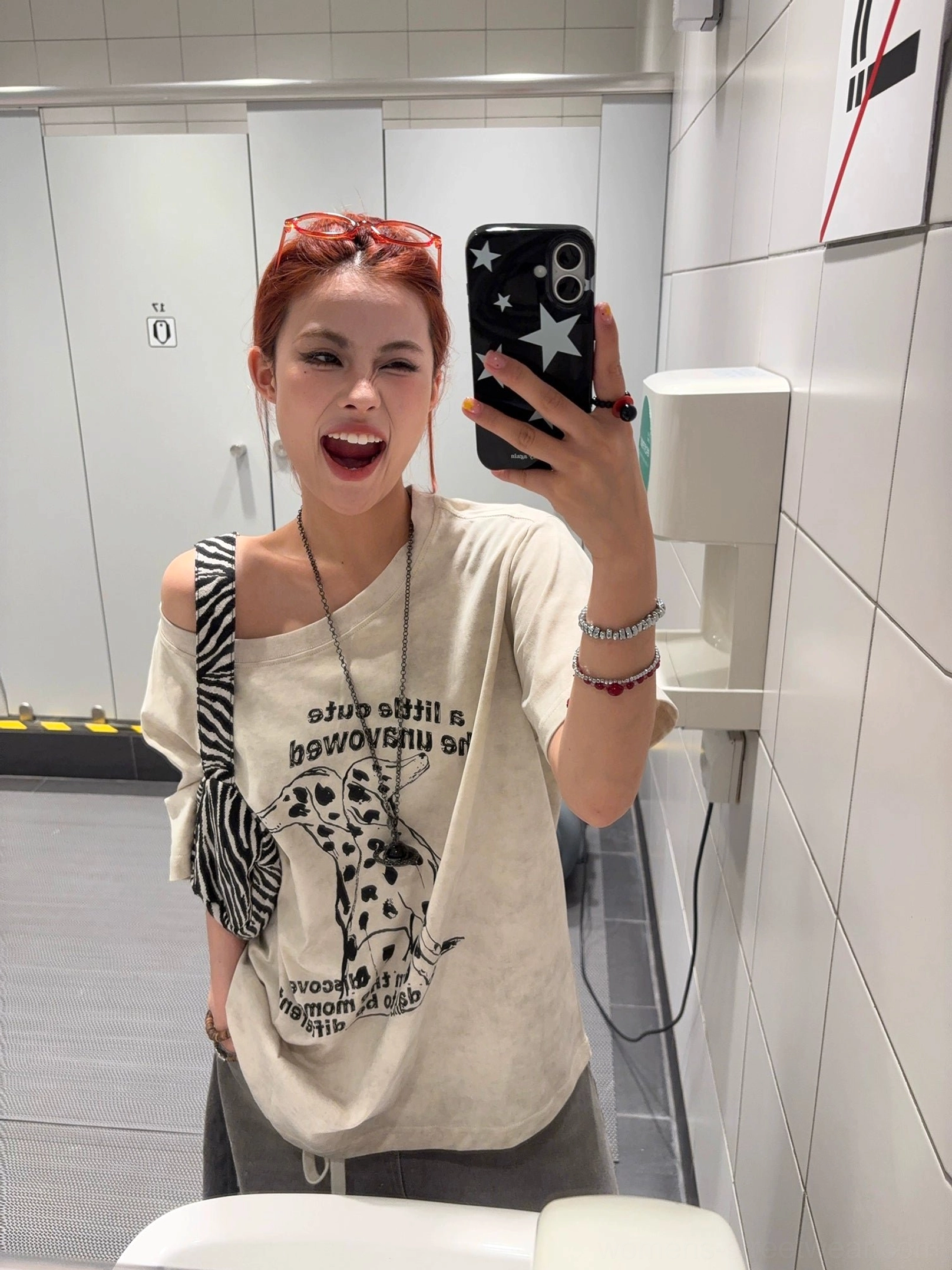 Close-up of washed apricot Dalmatian graphic T-shirt with reversed English lettering, one-shoulder styling, sunglasses and layered jewelry