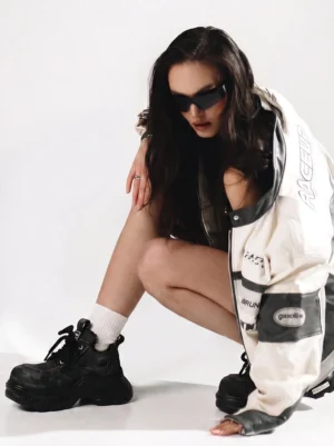 Female model wearing washed black denim chunky platform sneakers with a racing streetwear jacket in studio
