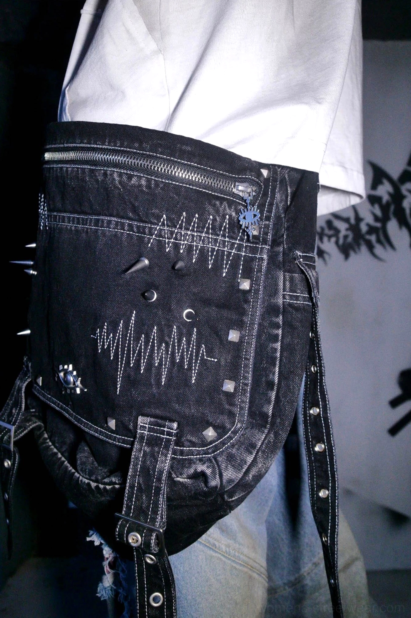 Front close-up of washed black denim cyberpunk crossbody bag with rivet-trimmed edges heartbeat embroidery eye badge and metal ornaments