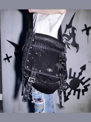 Close side view of washed black denim cyberpunk crossbody utility bag with heartbeat embroidery rivets eye badge and adjustable buckle straps
