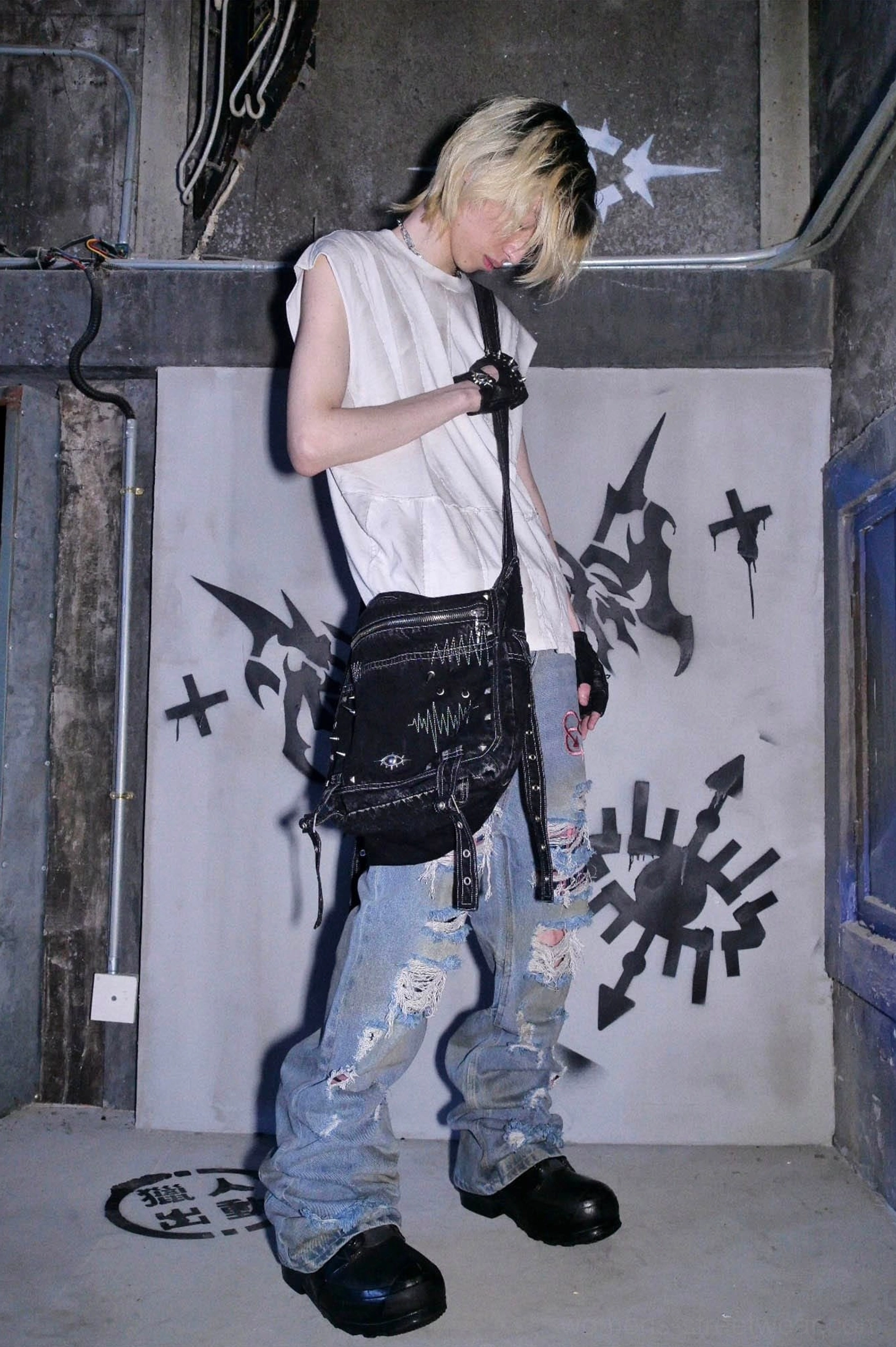 Full body side view of model styling a washed black denim cyberpunk crossbody utility bag with ripped denim streetwear outfit