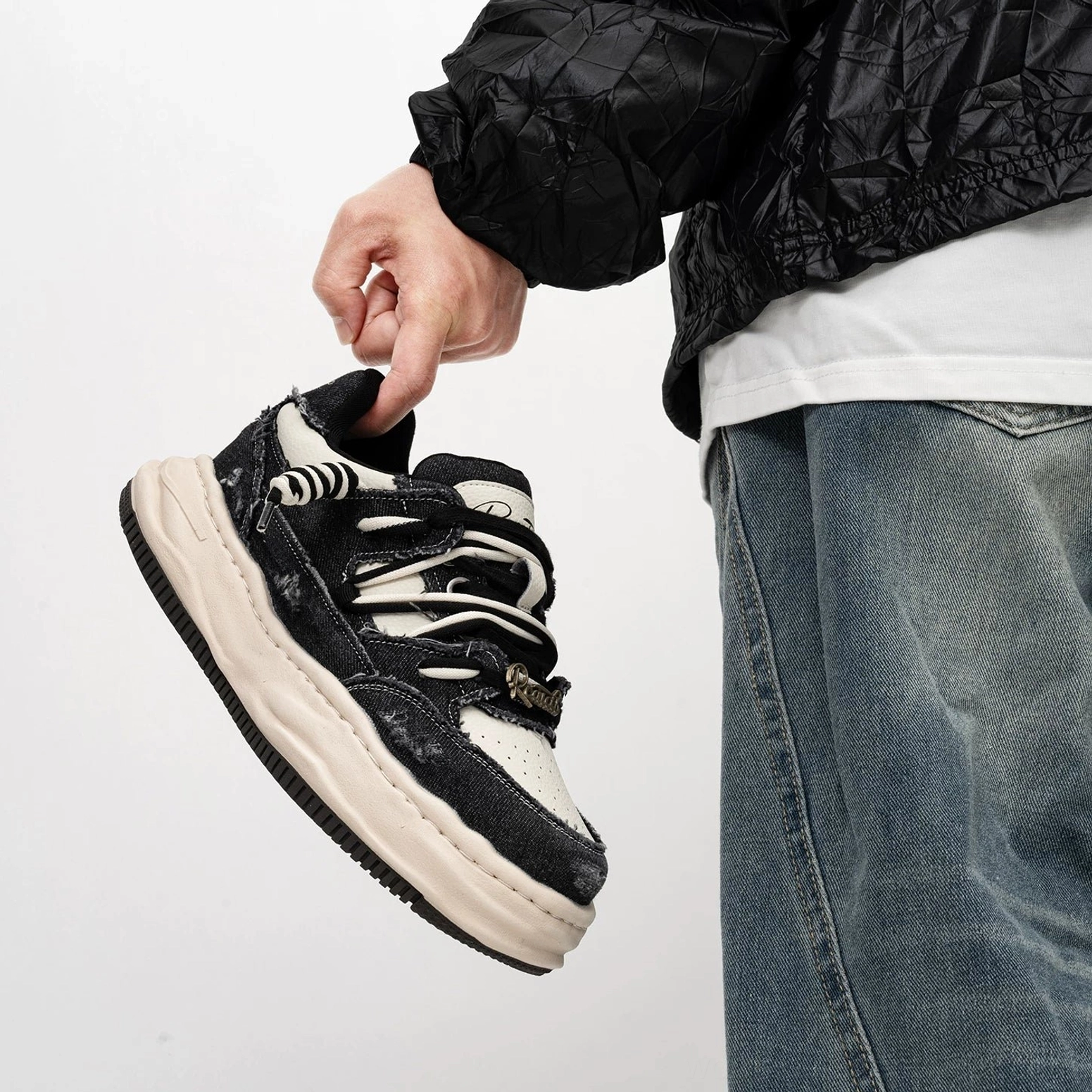 Washed black distressed canvas sneakers with contrasting white platform midsole and metal lace hardware held in a streetwear styling shot