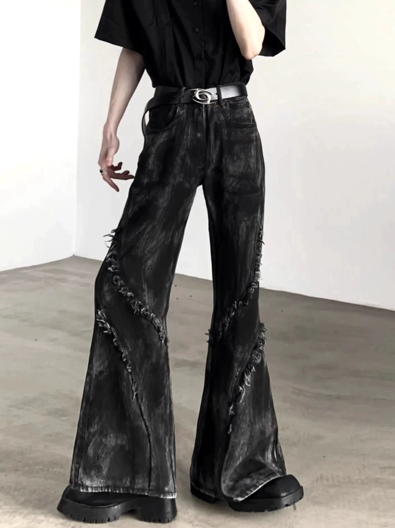Front-side view of washed black flared denim jeans with distressed diagonal seams, wide hems, belt loops, and visible front pockets